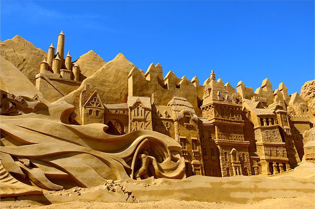Sandskulptur af bygninger, en ridder og flammer fra en drage